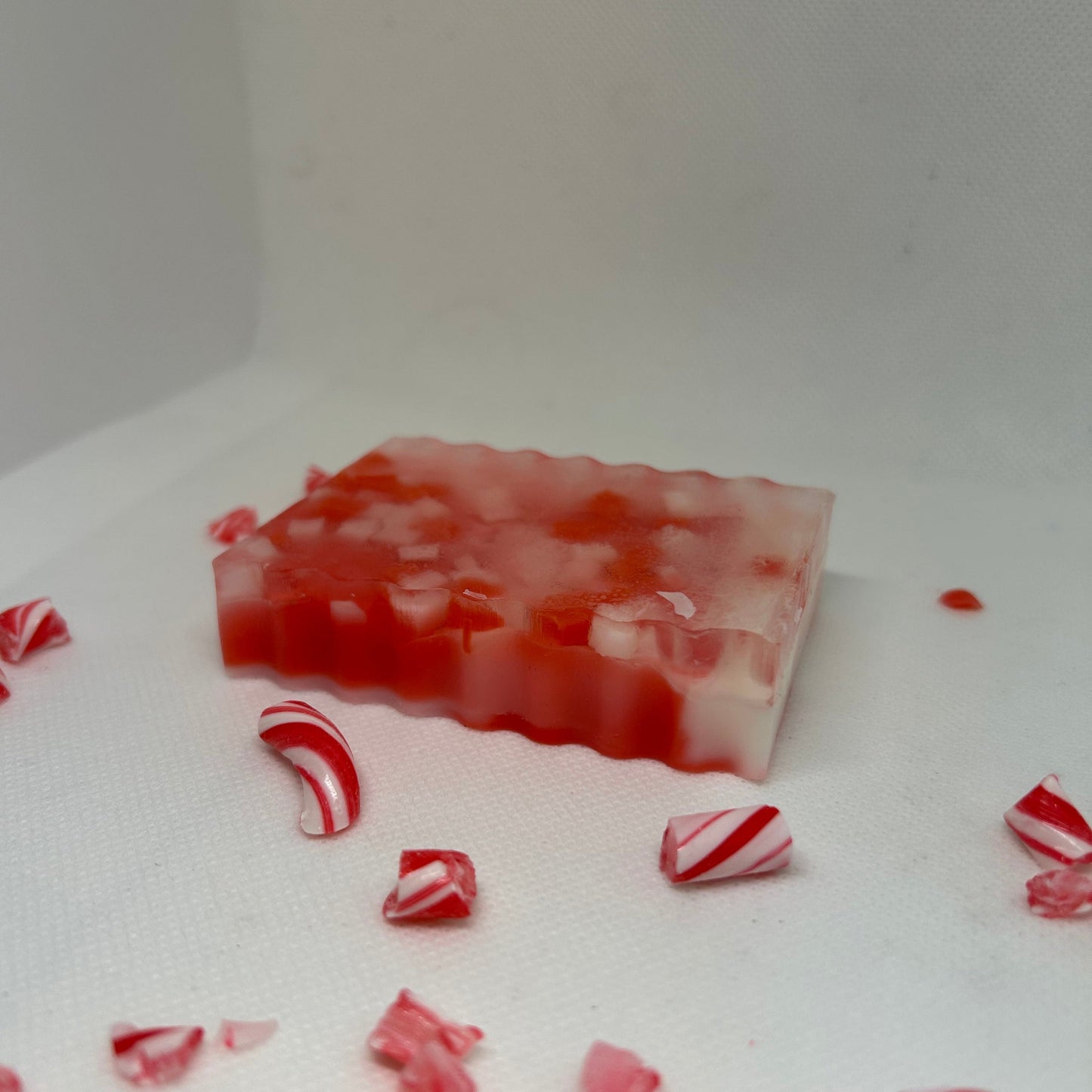 Frosted Cane peppermint soap with red and white layers, surrounded by crushed candy cane pieces, perfect for holiday gifts.