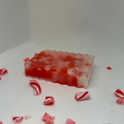 Frosted Cane peppermint soap with red and white layers, surrounded by crushed candy cane pieces, perfect for holiday gifts.